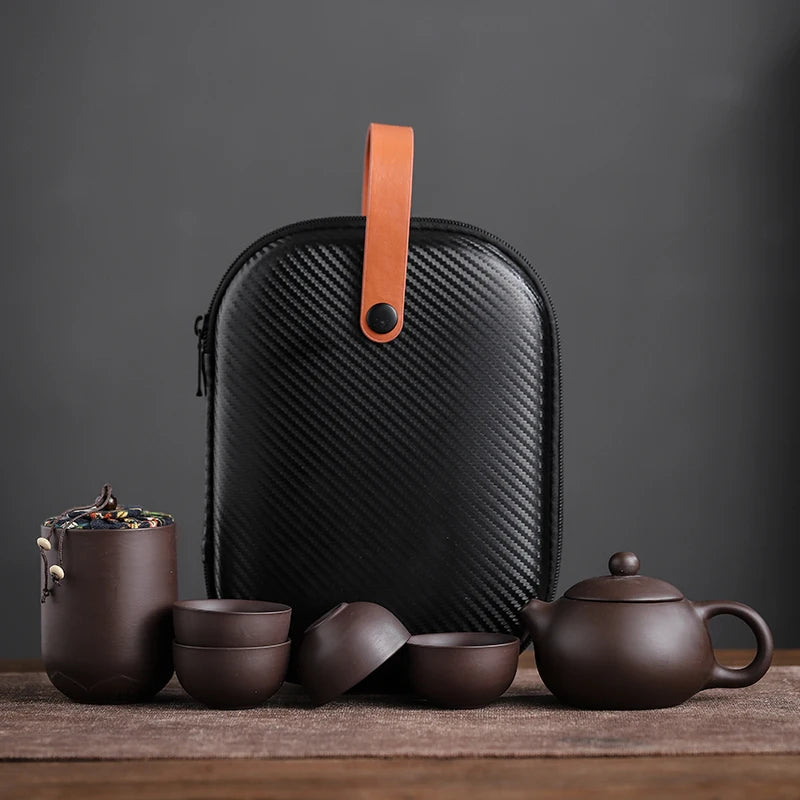 Set of brown ceramic tea pots and cups with a black carbon fiber case on a dark background