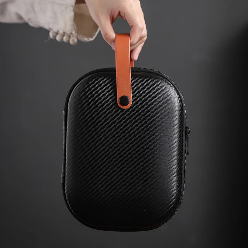 Black hard-shell travel case with orange handle held by a hand on a dark background