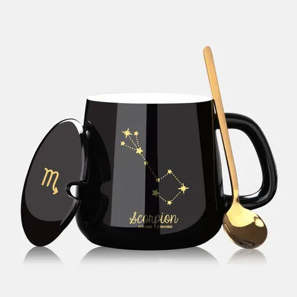 Black mug with Scorpio constellation design, gold spoon, and lid on a white background