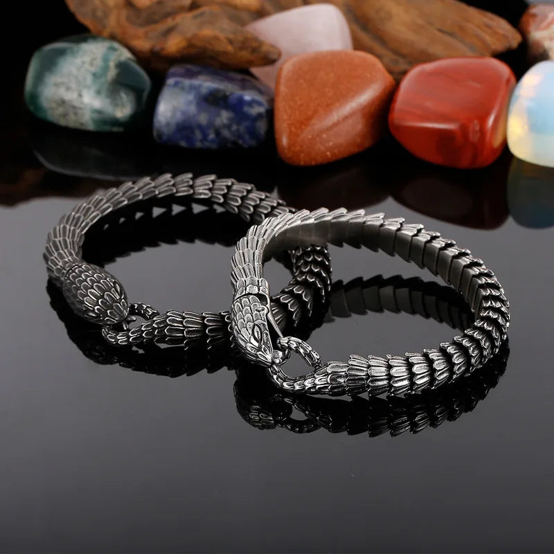 Silver snake bracelet on a reflective surface with colorful stones in the background